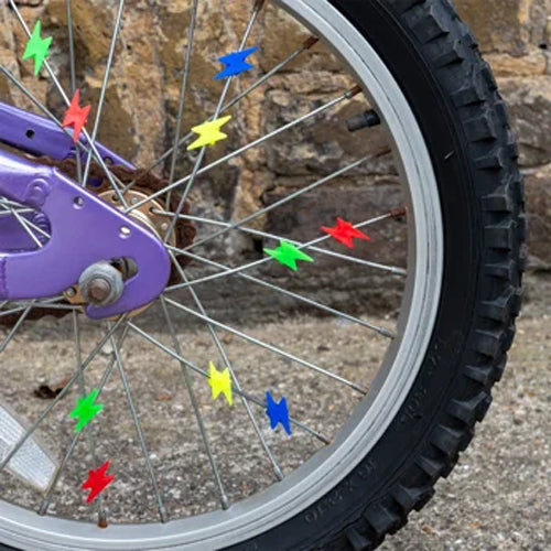 Close-up of a bicycle wheel with colorful stars attached to the spokes, against a stone wall background.