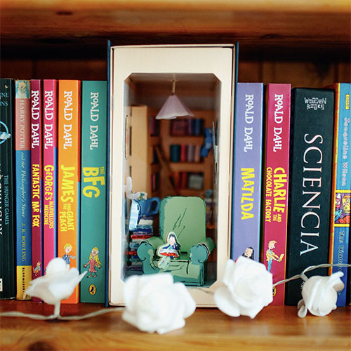 Book-shaped shelves with miniature furniture and decor inside, resembling a cozy room.