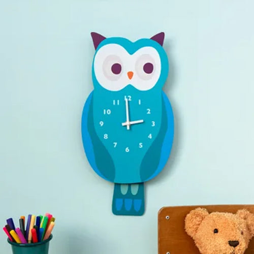 Blue owl-shaped wall clock on a light blue background with a teddy bear and coloring books.