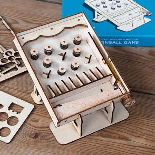 Wooden pinball game kit on a wooden surface with components and instructions.